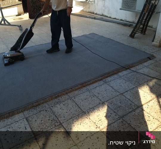 אדם מנקה שטיח עם שואב אבק חשמלי